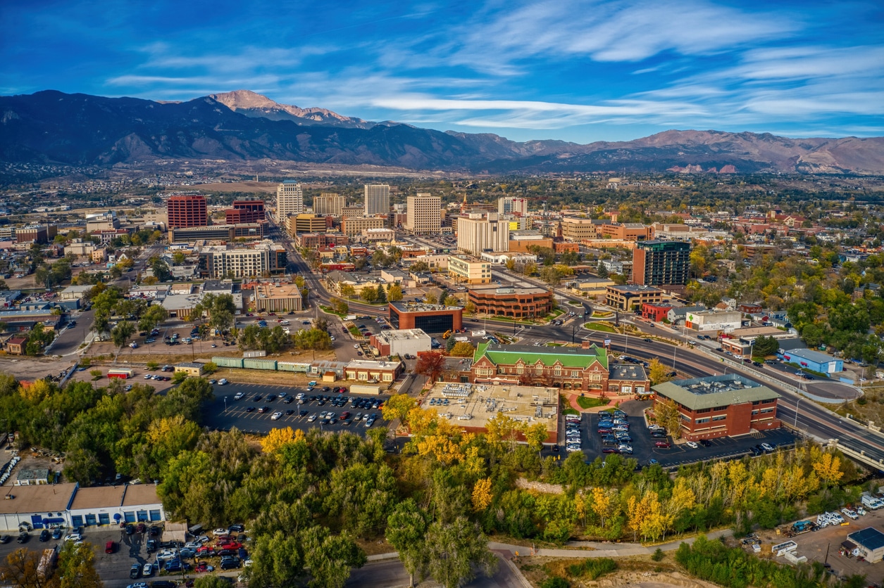 Aerial view of Colorado Springs with downtown buildings, autumn foliage, and mountains in the background