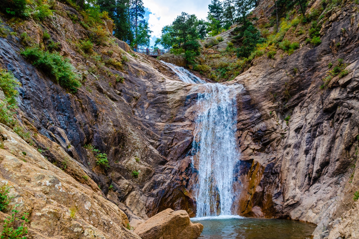 Seven Falls in Colorado Springs with cascading waterfalls down a rocky canyon into a pool, framed by trees and cliffs