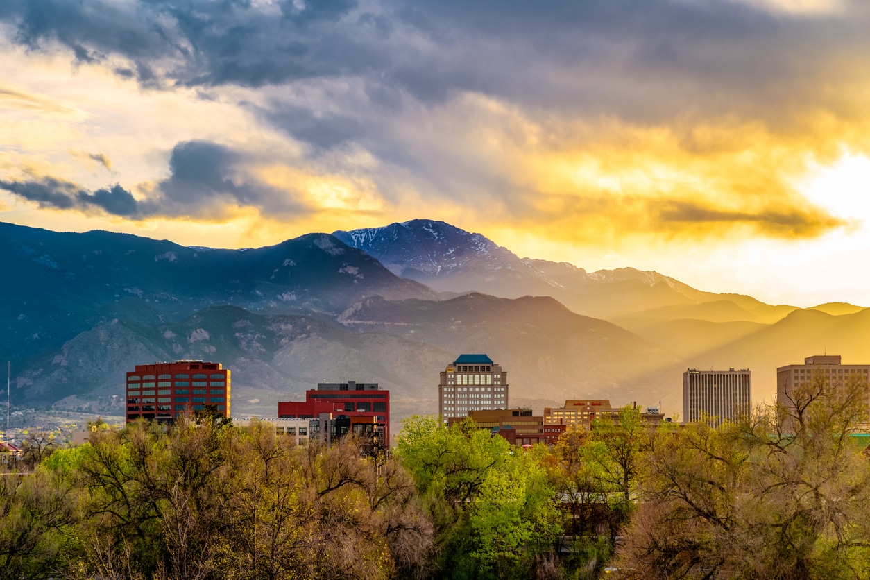 Colorado Springs downtown skyline at dusk with Pikes Peak beyond, glowing under a golden sunset