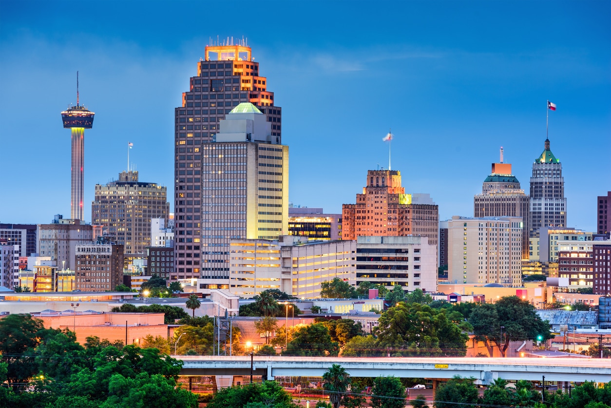 San Antonio skyline at dusk with Tower of the Americas, downtown skyscrapers, bridge, and green trees