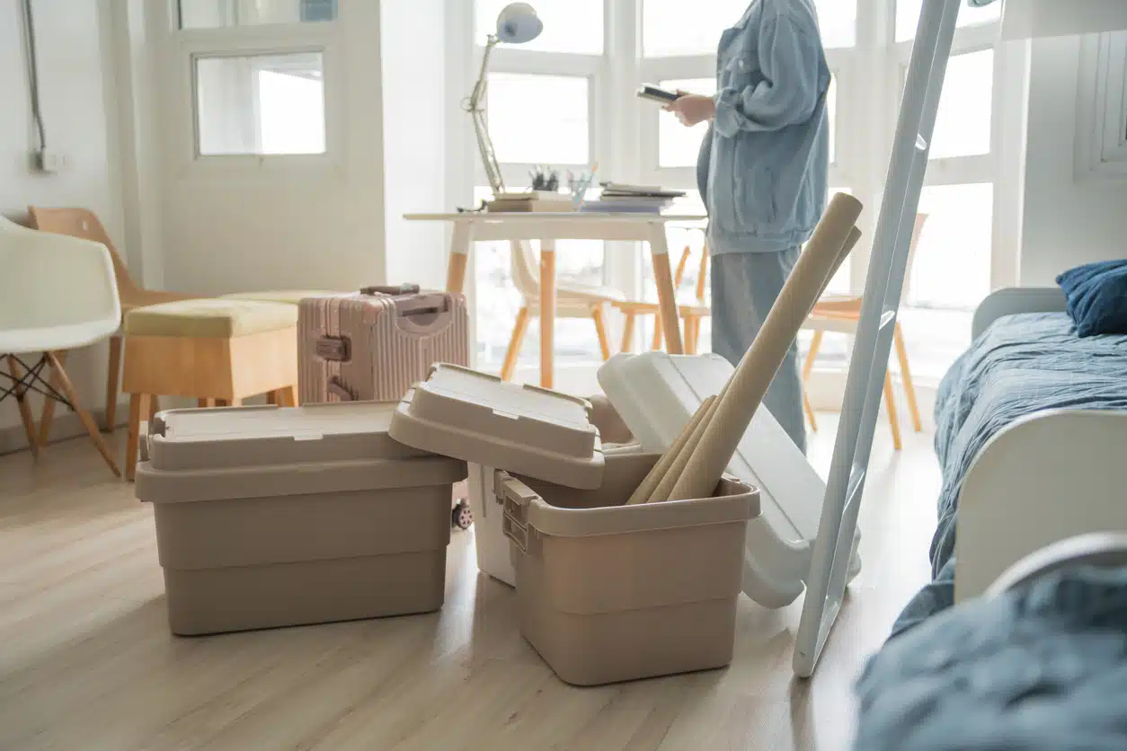 Student asian woman organize room unpack in dorm room college student moving to new university dormitory or preparing to move out. Plastic storage bins and luggage on the floor of a bright room as a person prepares for a move or unpacks belongings