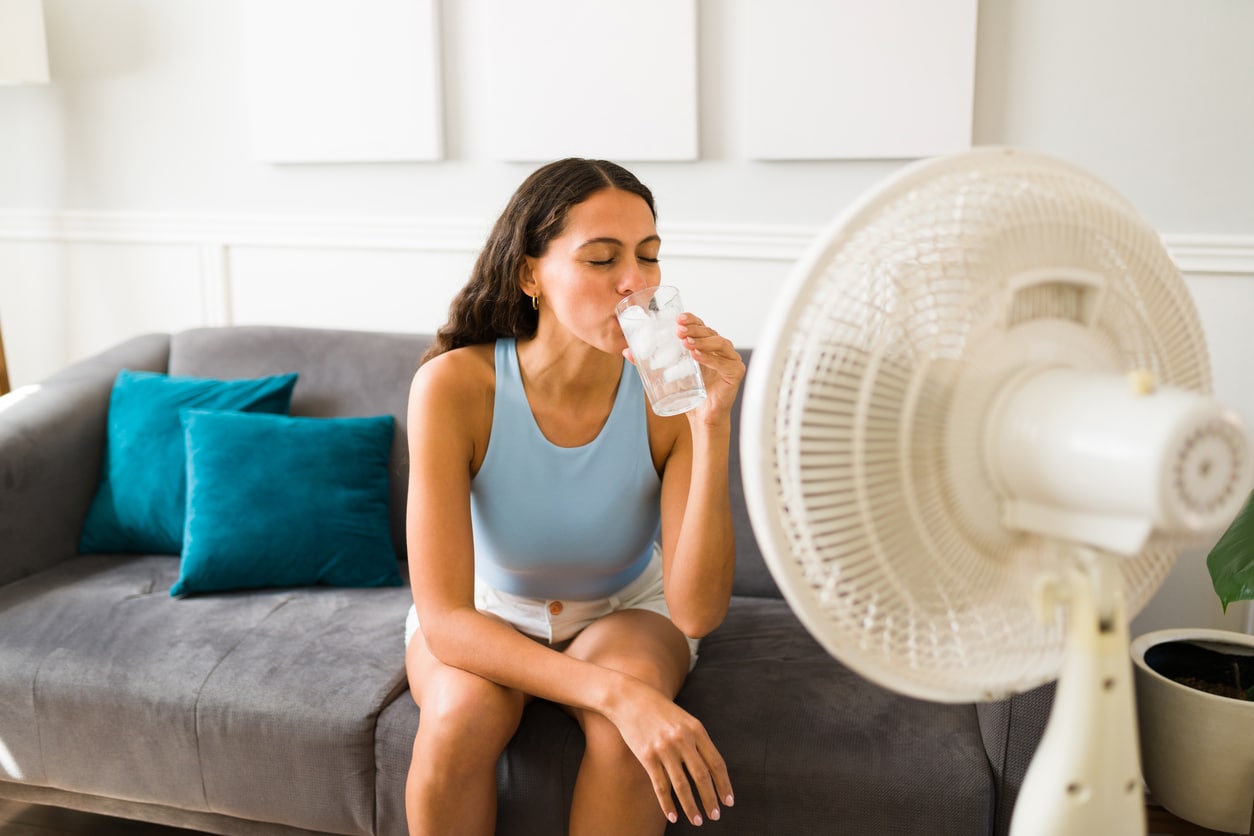 Woman enjoying a cold drink in front of the fan Woman cooling off with cold water in front of a fan while moving during summer