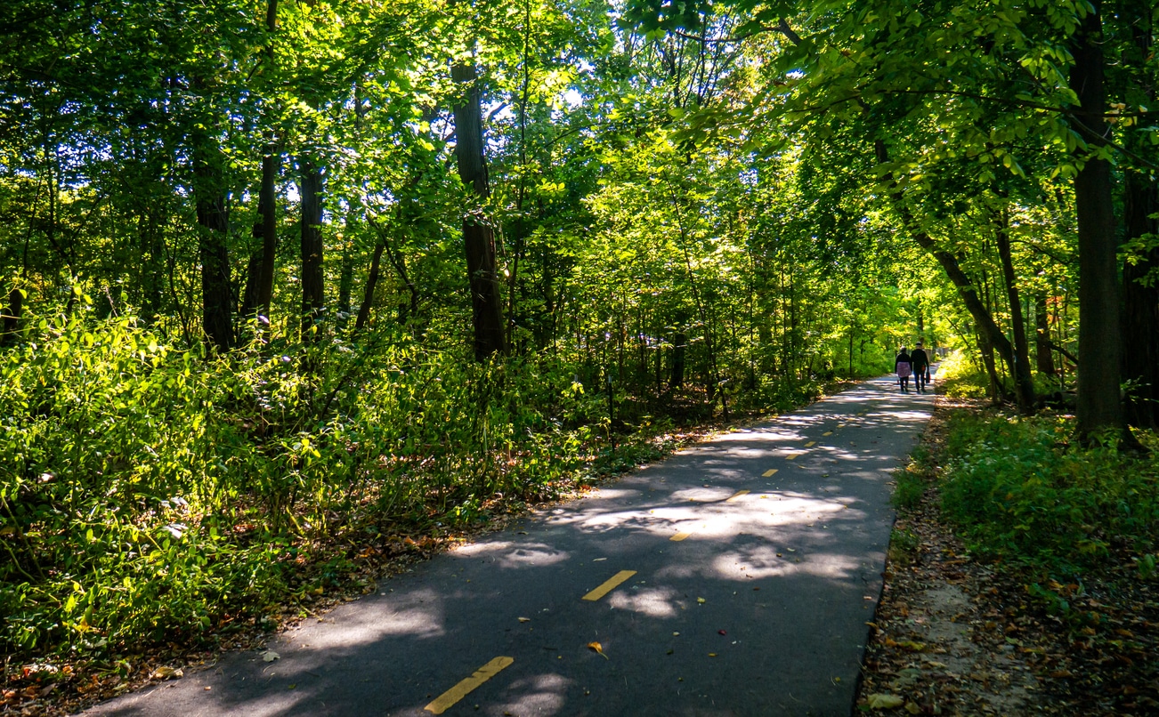 The Old Putnam Trail in Van Cortlandt Park, the Bronx, New York City Paved path through lush forest in Van Cortlandt Park, Bronx, with two people walking in the distance