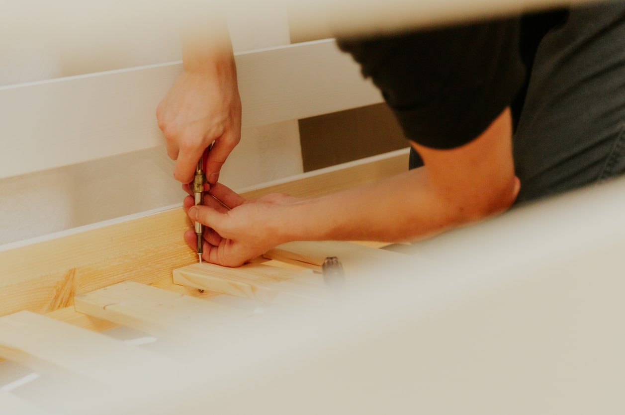 A young man installs a bunch of frame boards on a bunk bed. Close-up of hands using a screwdriver to disassemble a wooden bed frame for moving
