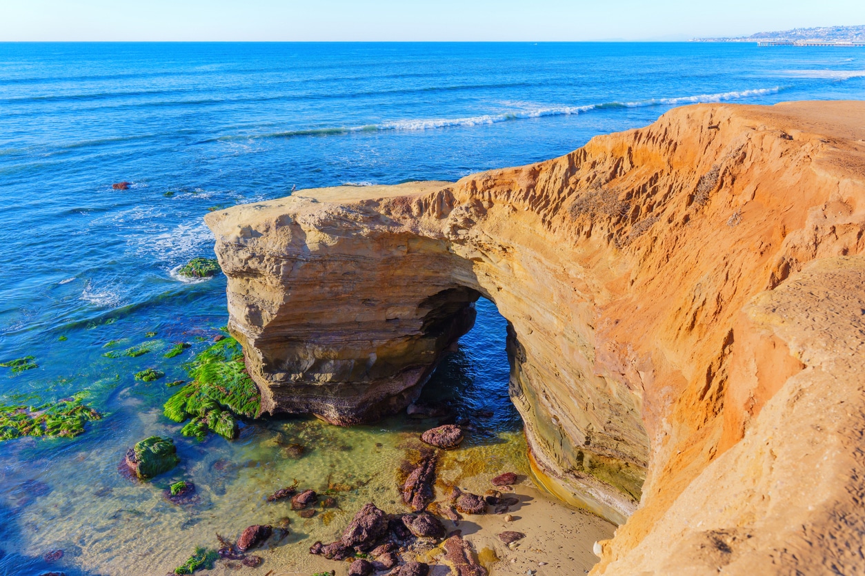 Sandstone arch on San Diego’s coast, framed by tide pools, beach, and the Pacific Ocean under a bright sky
