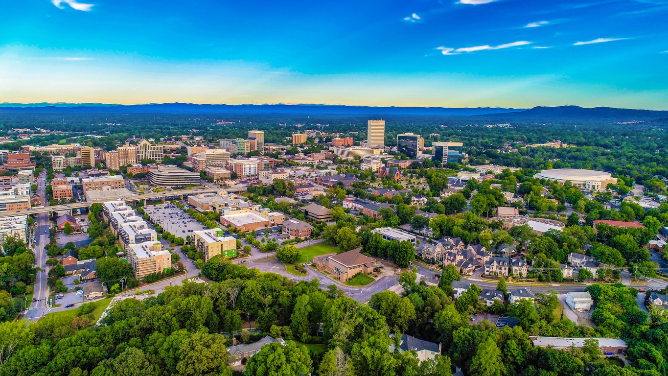 Aerial view of vibrant downtown Greenville, South Carolina, surrounded by lush green trees and distant mountains
