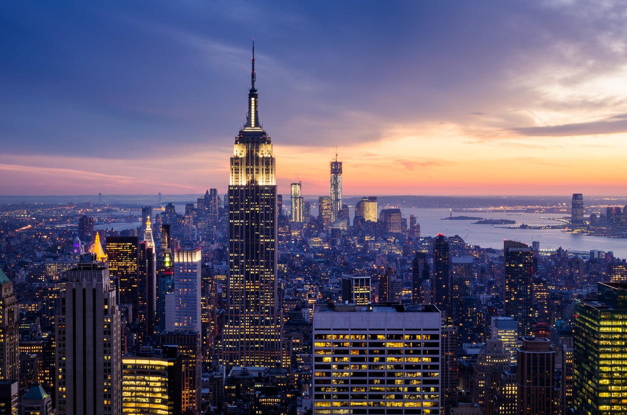 Empire State Building and NYC skyline at dusk, with city lights illuminated against a colorful sky