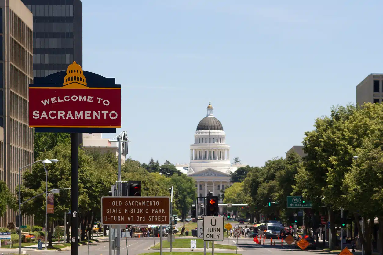 Welcome To Sacramento Welcome to Sacramento" sign with the California State Capitol building visible in the background on a sunny day