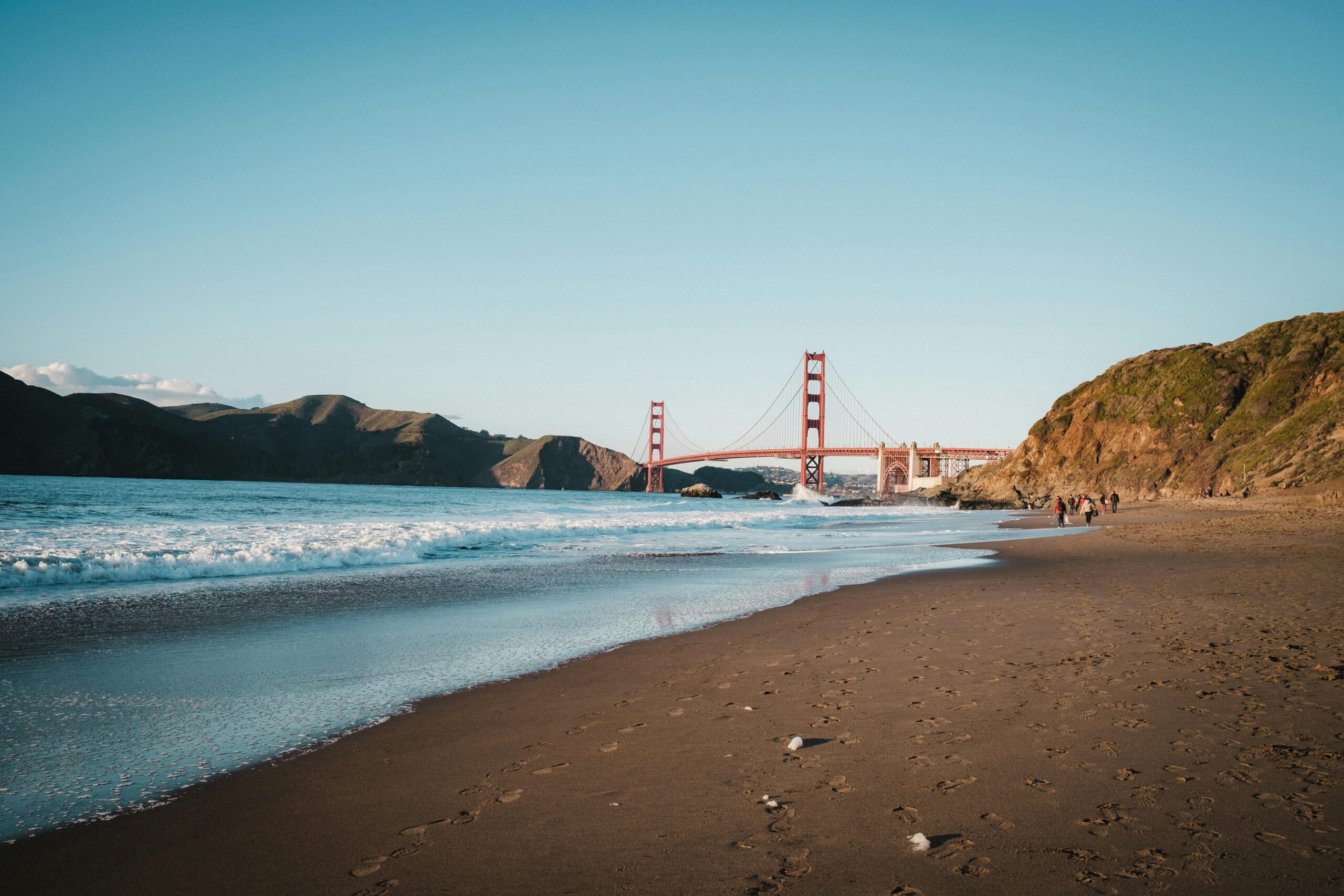 Golden Gate Bridge and Baker Beach in San Francisco with waves gently washing ashore under a clear blue sky