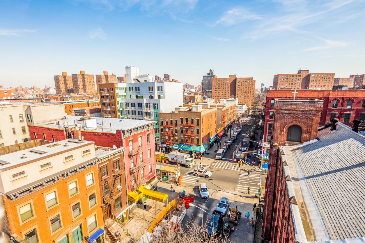 Lively East Harlem street in NYC with cars, pedestrians, and brick buildings under a bright clear sky