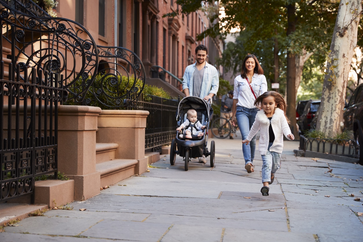 : A family living in Brooklyn walks down the sidewalk by brownstone homes