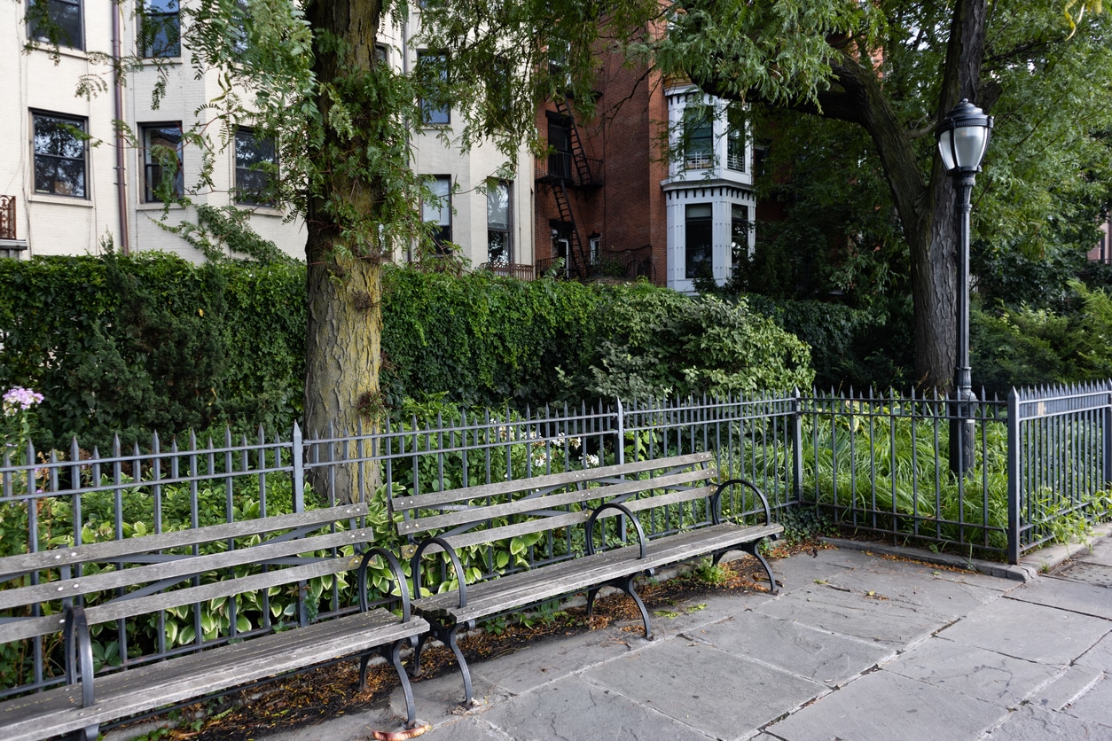 A tree-lined Brooklyn Heights street with historic brownstones, a park bench, and a glowing lamppost at dusk