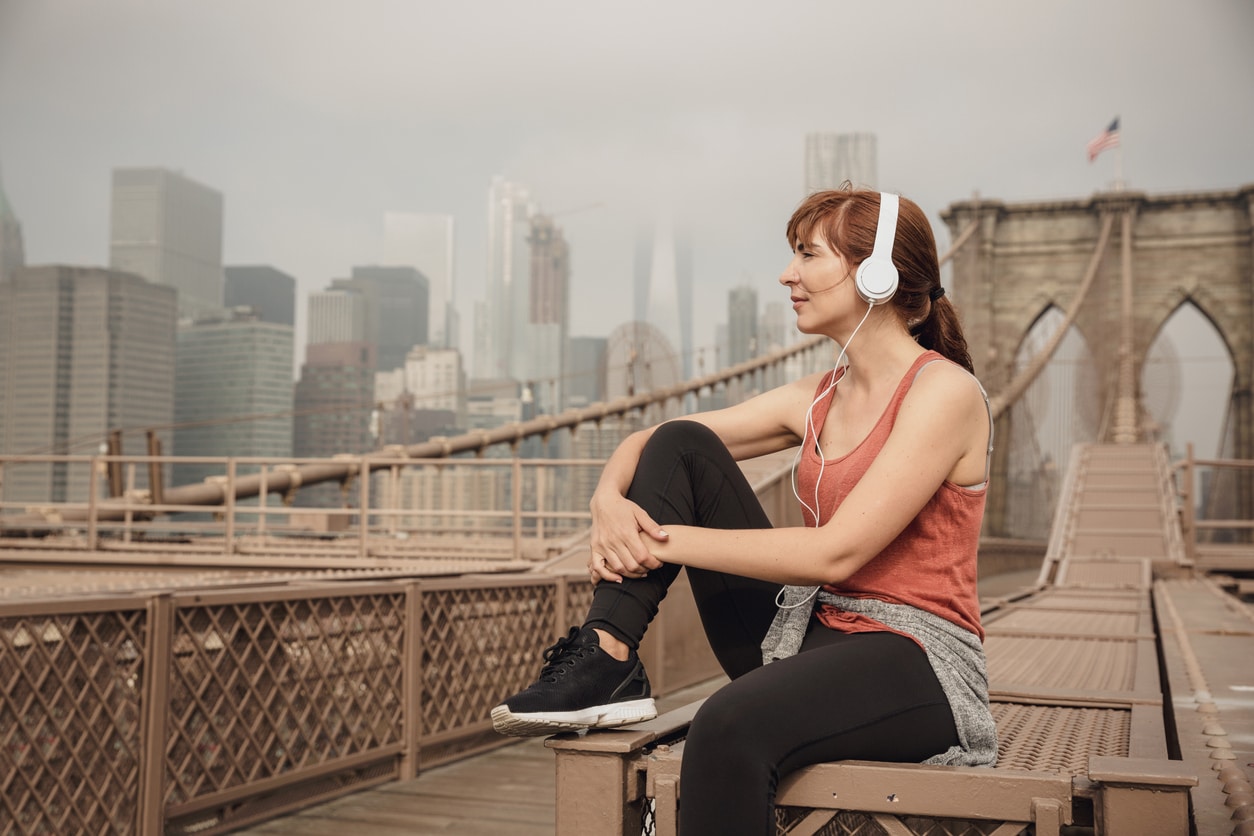 A woman in athletic wear and headphones sits on the Brooklyn Bridge after moving to Brooklyn
