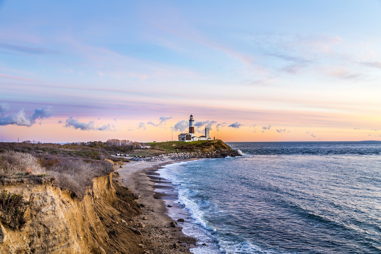 Montauk Point Lighthouse perched on Long Island cliffs at sunset, overlooking the ocean with waves on the beach