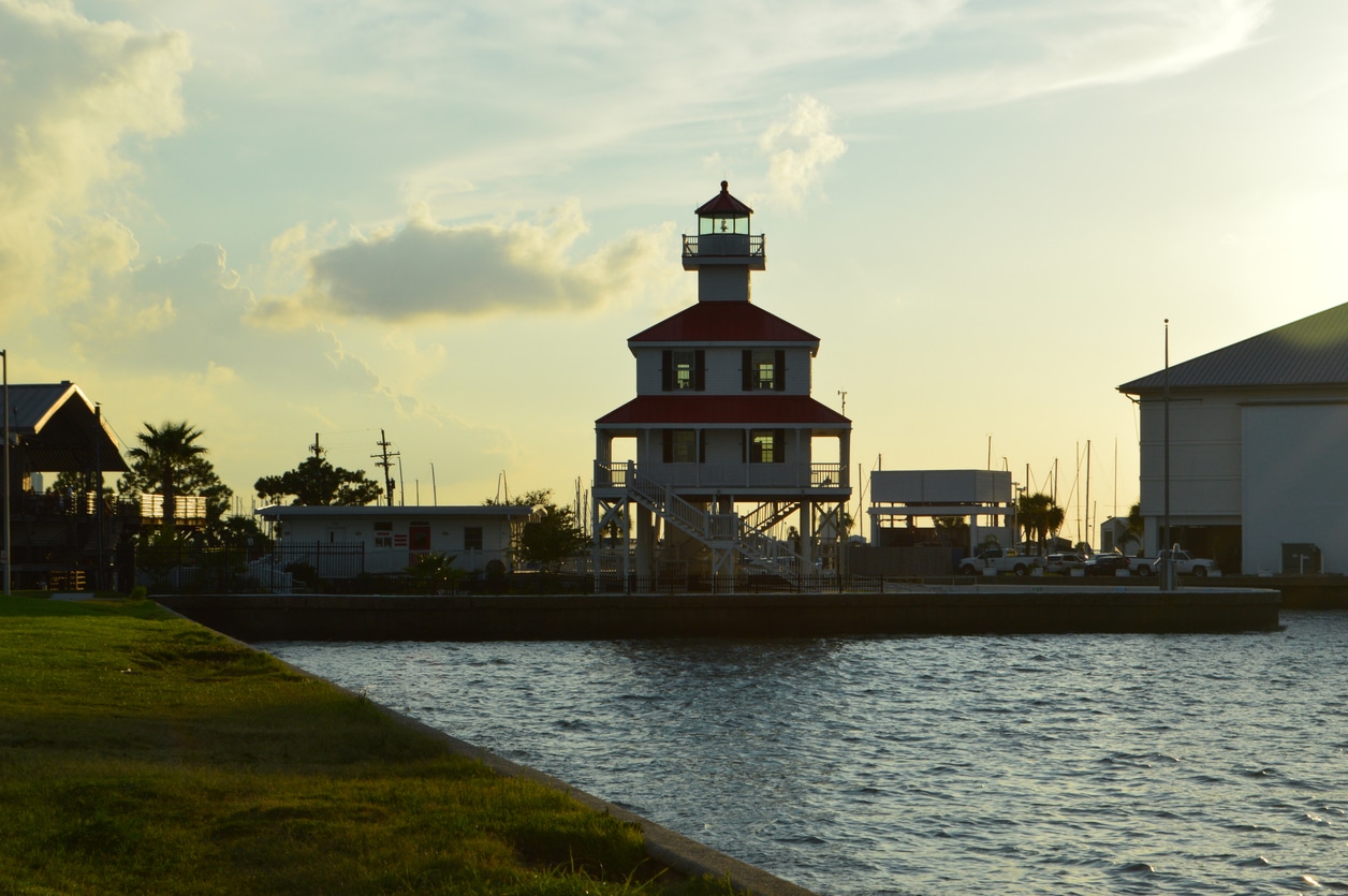 New Canal Lighthouse on Lake Pontchartrain at sunset, with calm water, boats, and city buildings