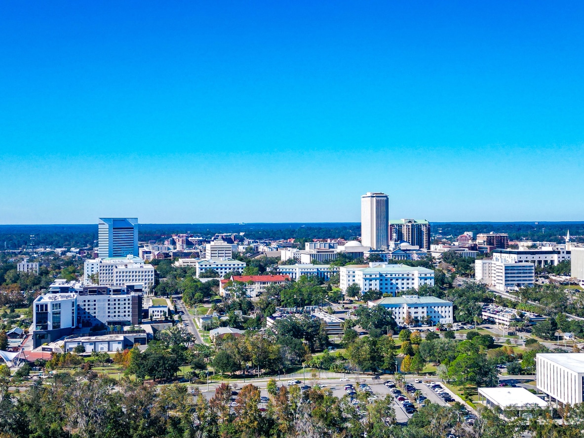 Aerial view of Tallahassee, Florida, with the State Capitol building and city structures amid green landscapes