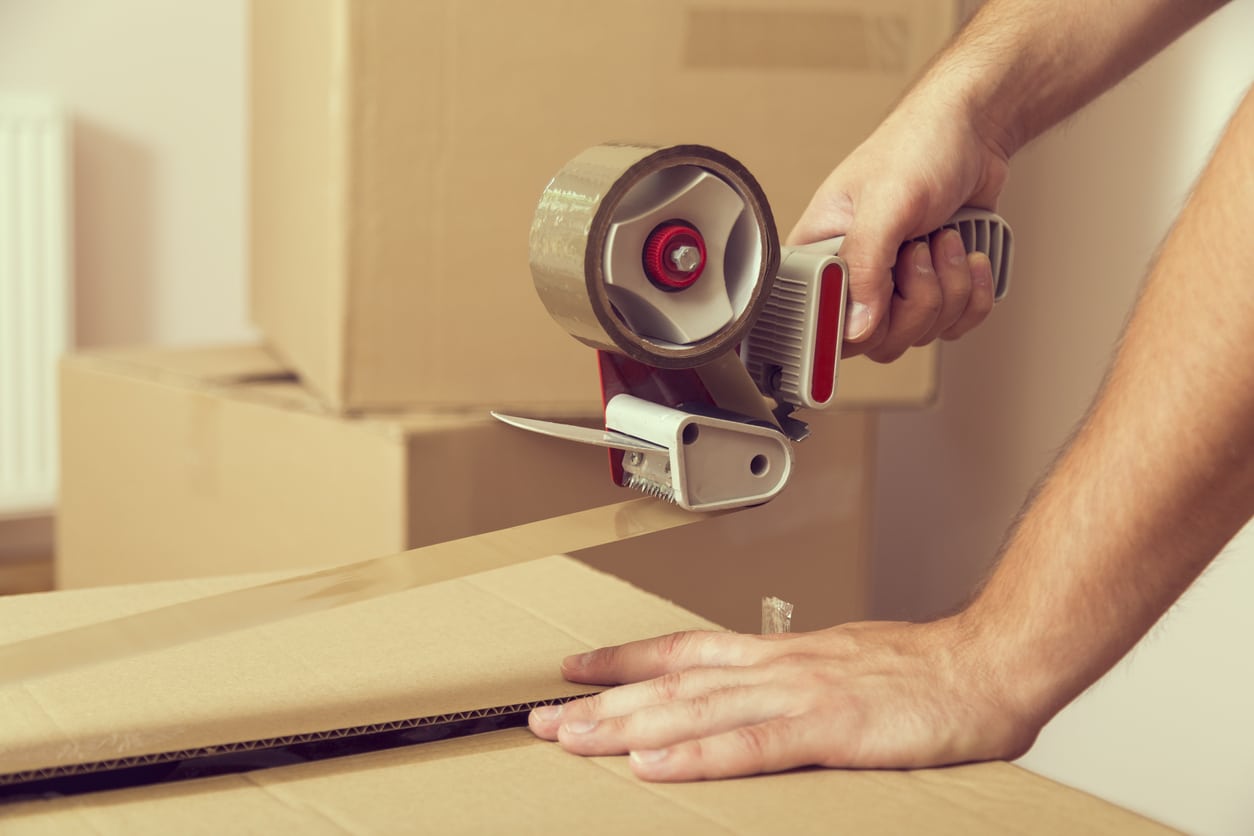 Close-up of hands using a tape dispenser to seal a cardboard moving box