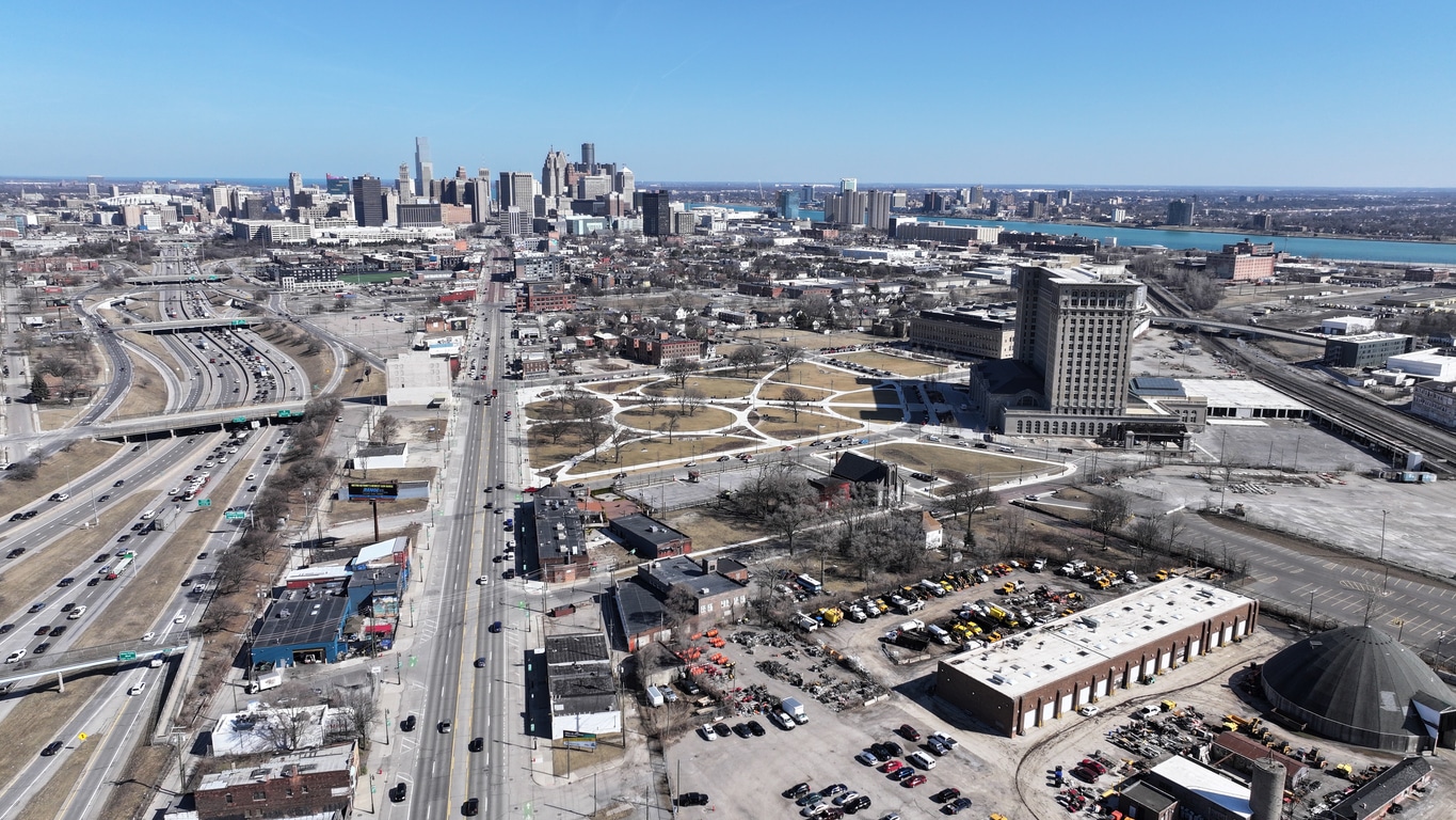 Aerial view of Detroit’s Michigan Central Station with city skyline and industrial areas under clear skies