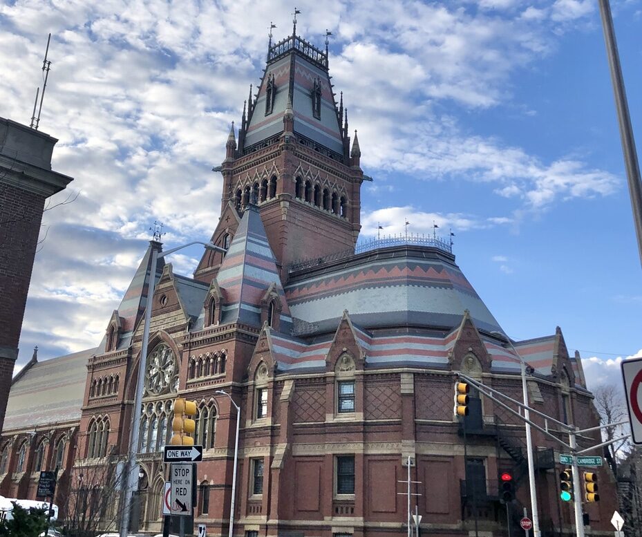 Harvard Square in Cambridge at dusk with historic brick buildings, glowing storefronts, and a lively street scene