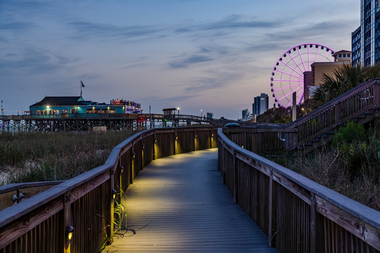 Night view of the Myrtle Beach boardwalk leading to a resort hotel and the illuminated SkyWheel in the background