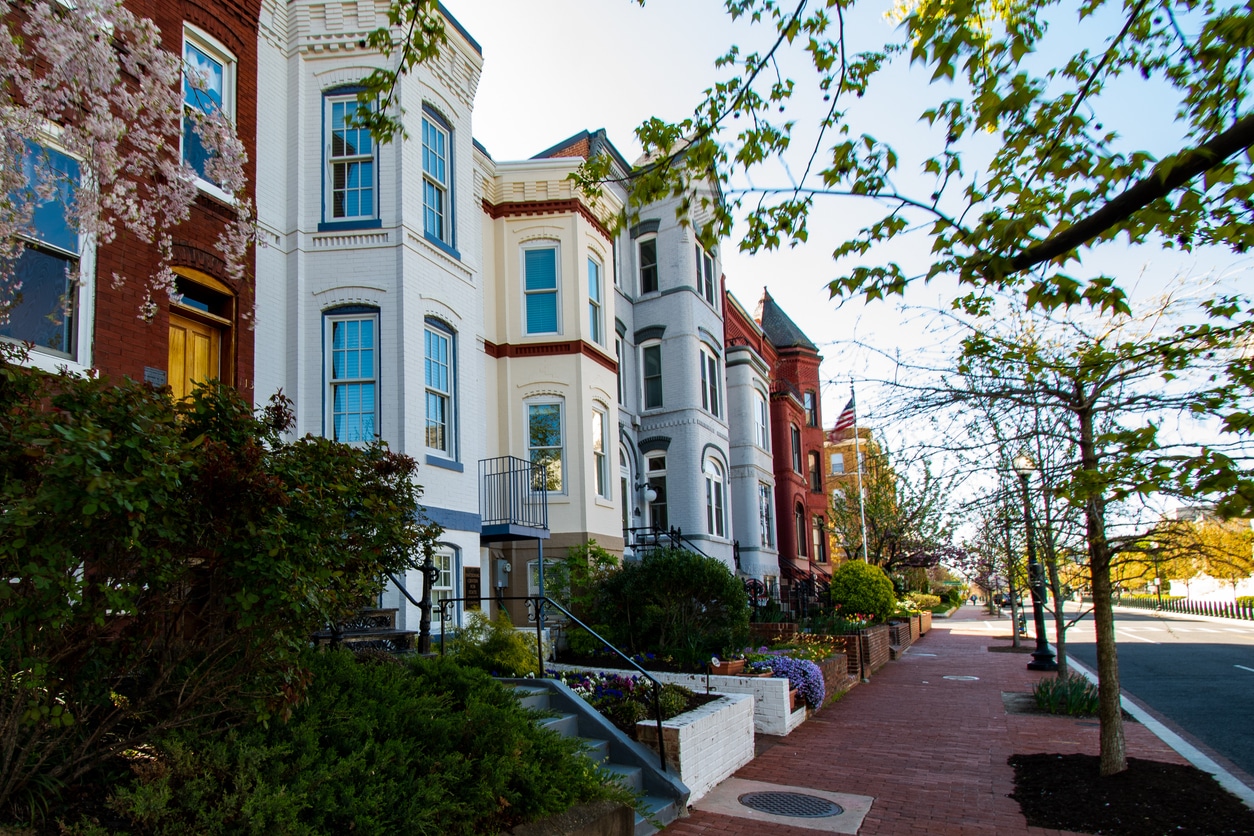 Colorful historic row houses with dark shutters line a tree-shaded brick sidewalk in Washington, D.C.’s Capitol Hill