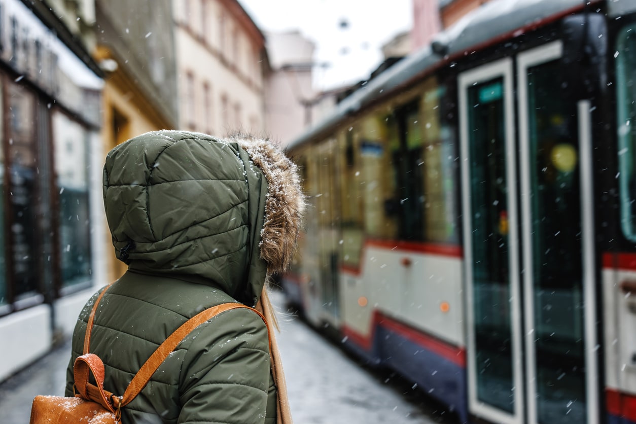  A person in a green winter parka waits for a tram on a snowy city street