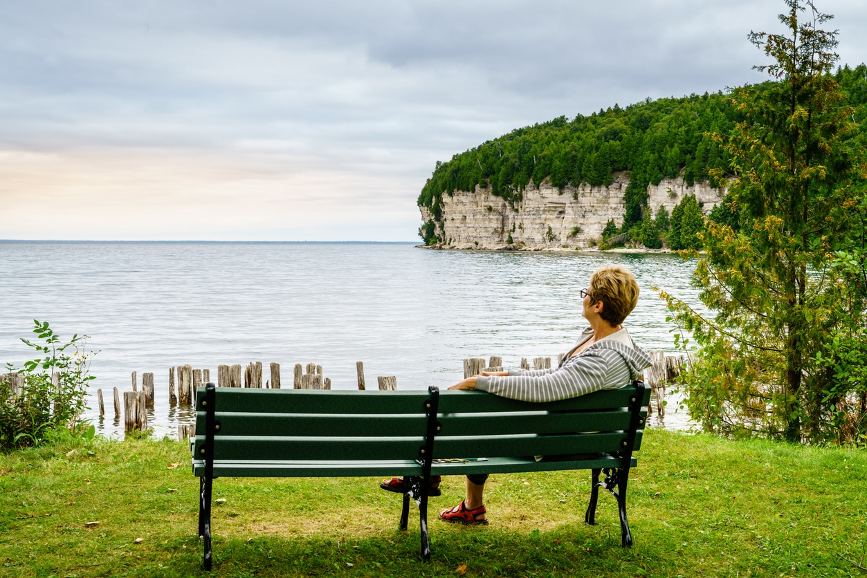 A woman enjoying living in Michigan as she sits on a bench overlooking Snail Shell Harbor at Fayette Historic State Park