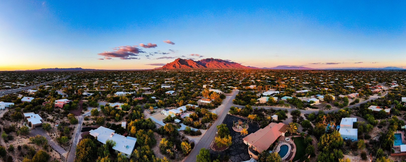 Aerial panorama of a Tucson, Arizona neighborhood at sunset, with the glowing Santa Catalina Mountains in the distance