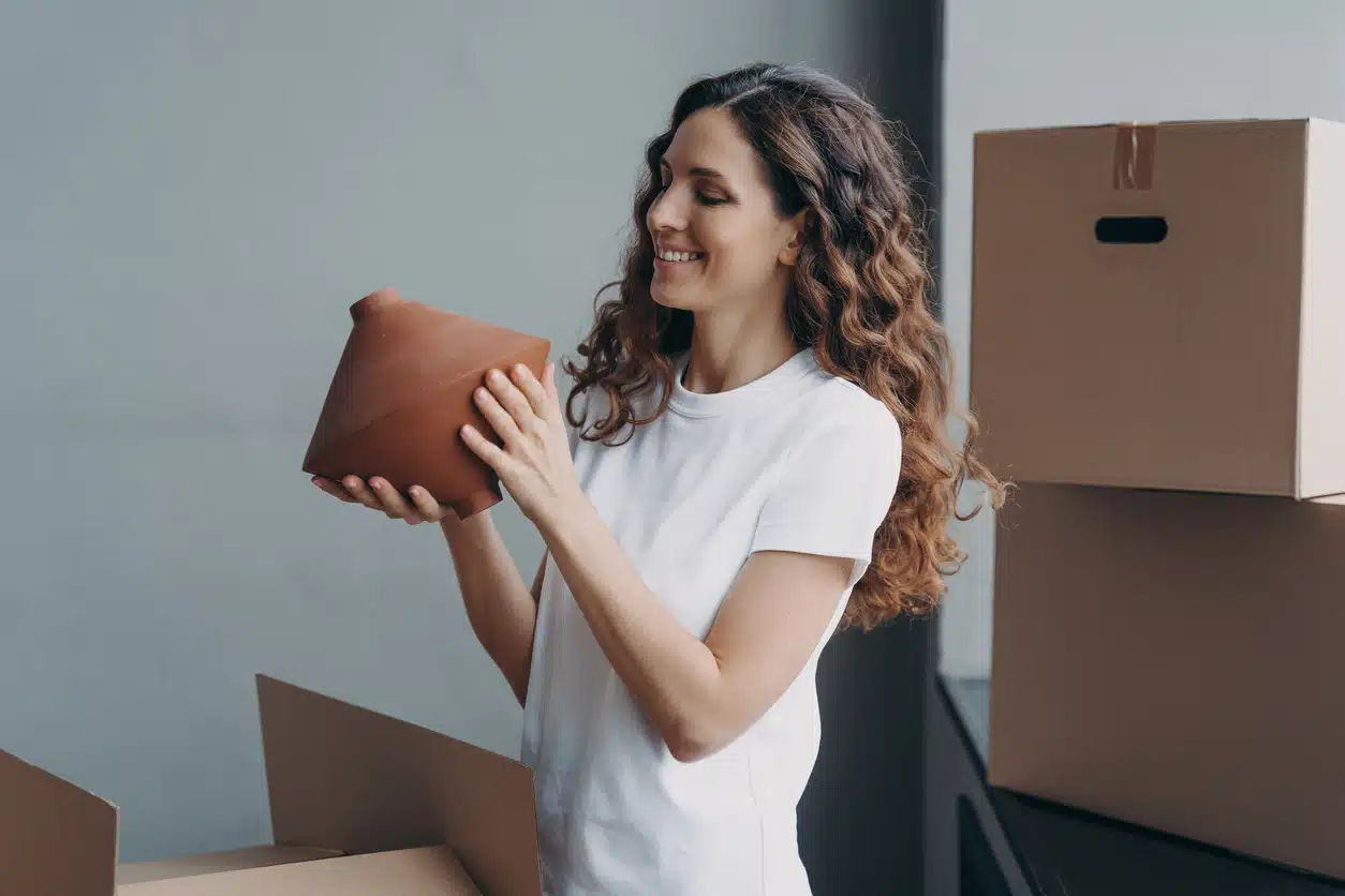 A woman holding a vase, surrounded by moving boxes, as she gets ready for moving with antiques