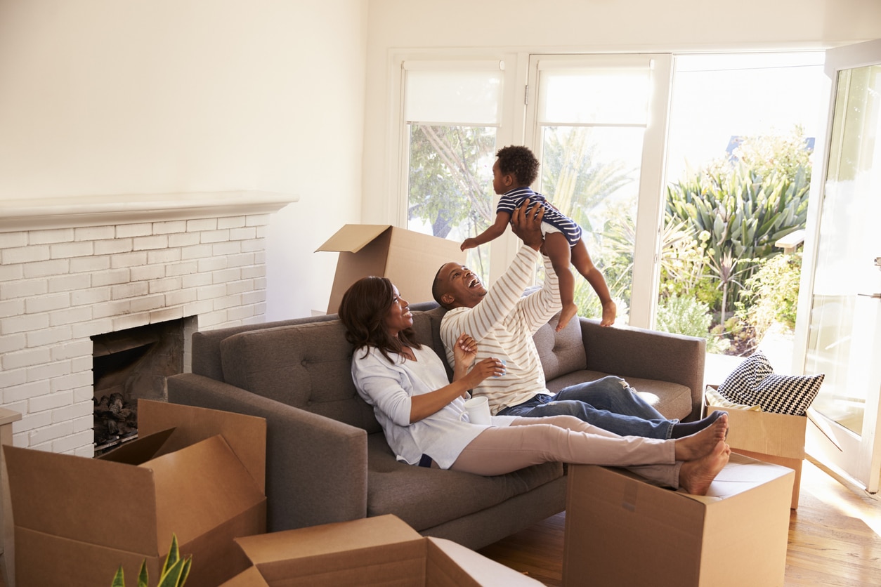 Parents Take A Break On Sofa With Son On Moving Day A husband and wife play with their baby surrounded by moving boxes in their new home