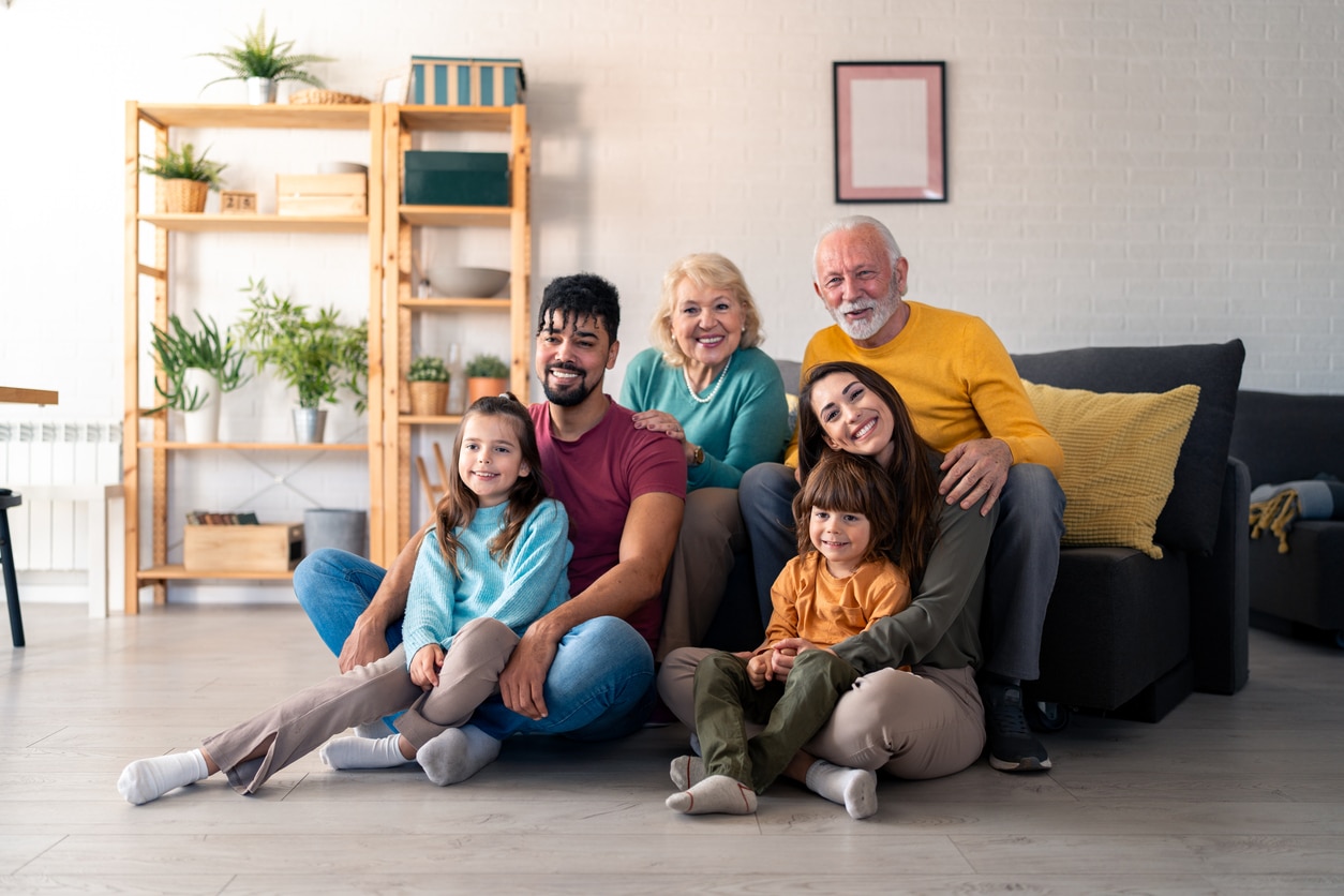 Multicultural Family Smiling Together in Modern Living Room With Bright Decor and Cozy Atmosphere A happy multi-generational family sits together in a living room, smiling at the camera