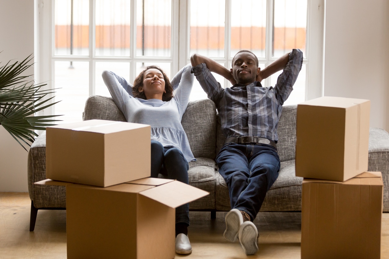A couple relaxes on a sofa surrounded by moving boxes after moving to another state to start over
