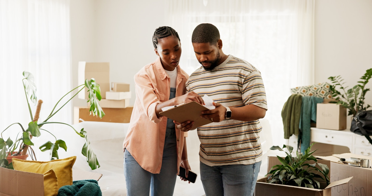 Boxes, clipboard and moving house with black couple in living room for planning or relocation. Checklist, conversation and real estate with people in home for discussion, packing or property task A couple reviews a checklist on a clipboard while surrounded by moving boxes in their new, sunlit home
