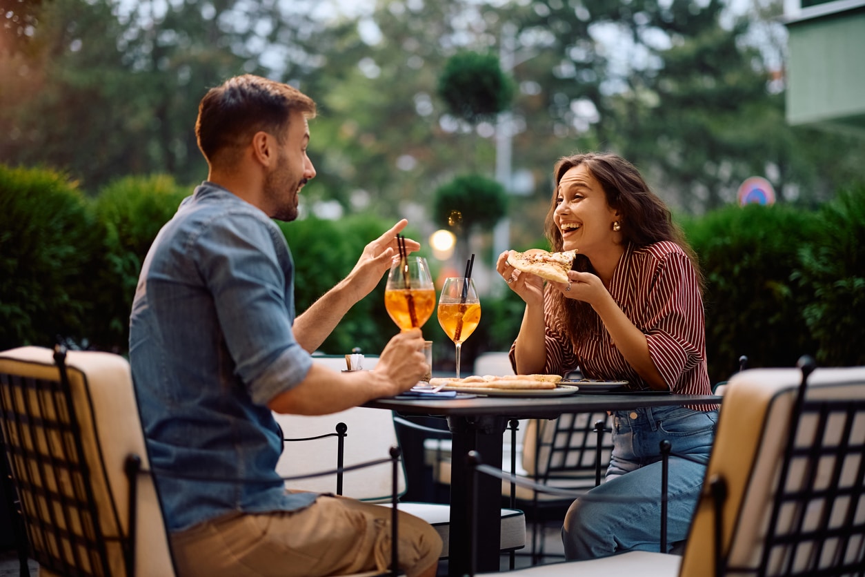 Cheerful couple talking while enjoying in lunch in pizzeria. A man and woman sit at an outdoor restaurant table after relocating for love