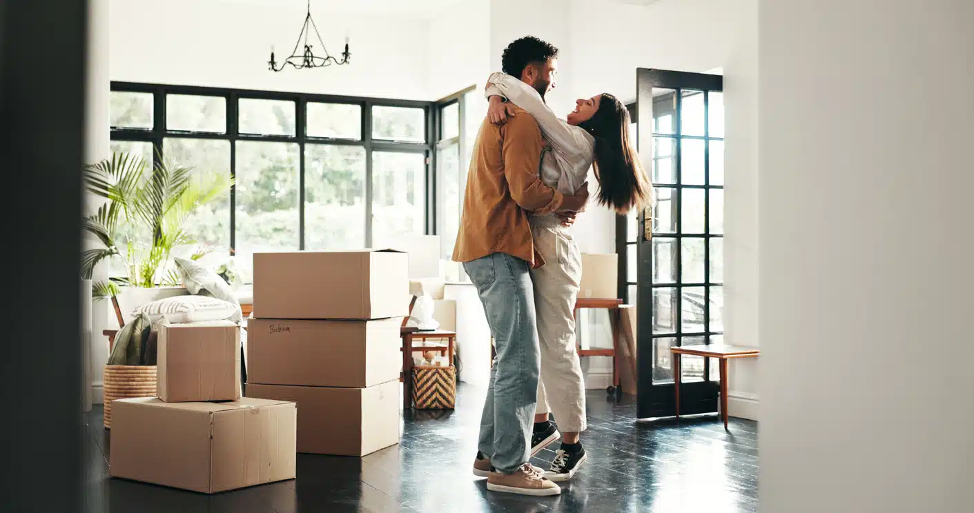A happy couple embraces and celebrates moving for a relationship, surrounded by moving boxes