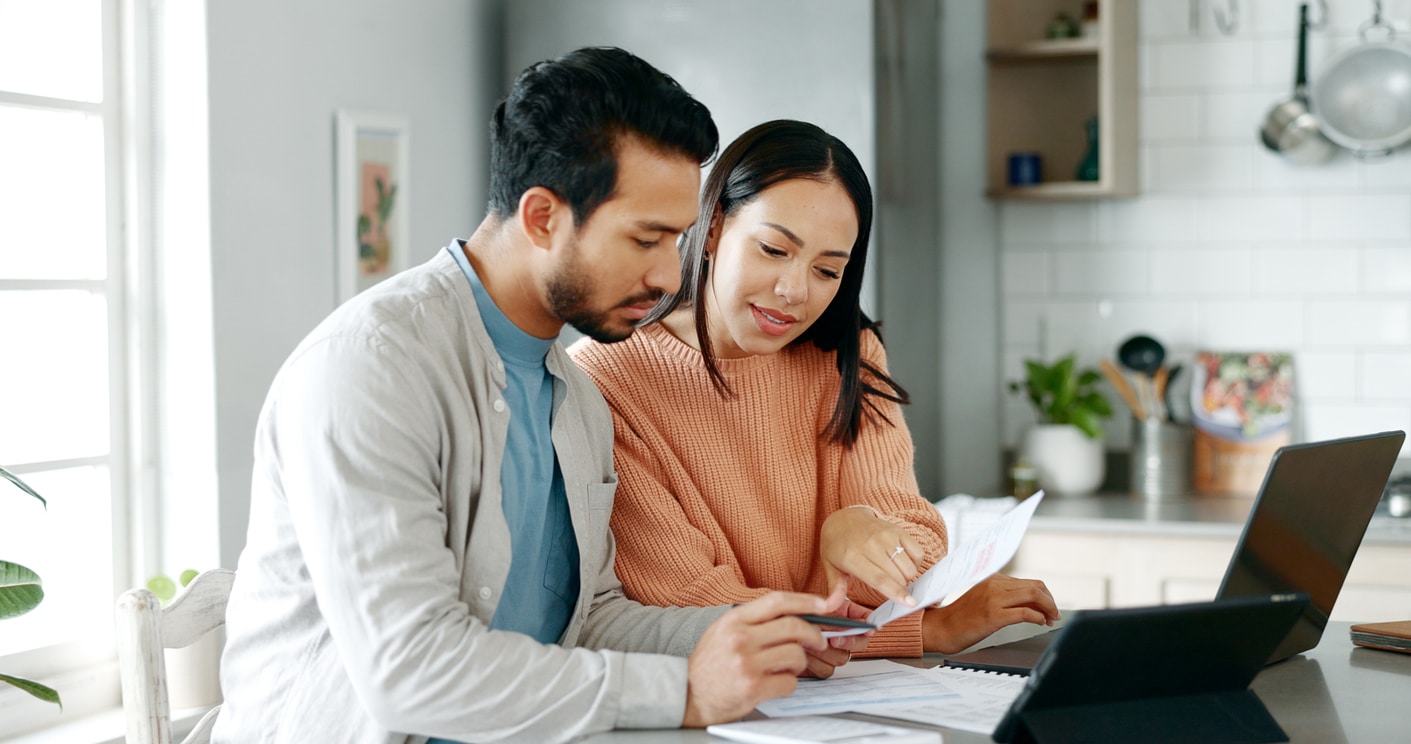 Kitchen, couple and discussion with document for finance, track expenses and laptop for budget goal. Conversation, man and woman with tax paper for checking, mortgage review or handle savings at home A couple sits at a kitchen table planning out moving in together, reviewing paperwork together with a laptop and tablet