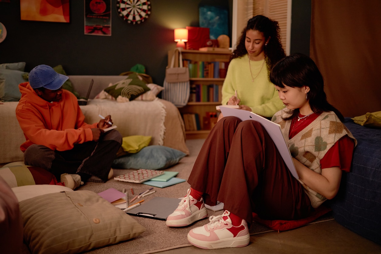 Three students sit on a bedroom floor, focused on studying after moving for education