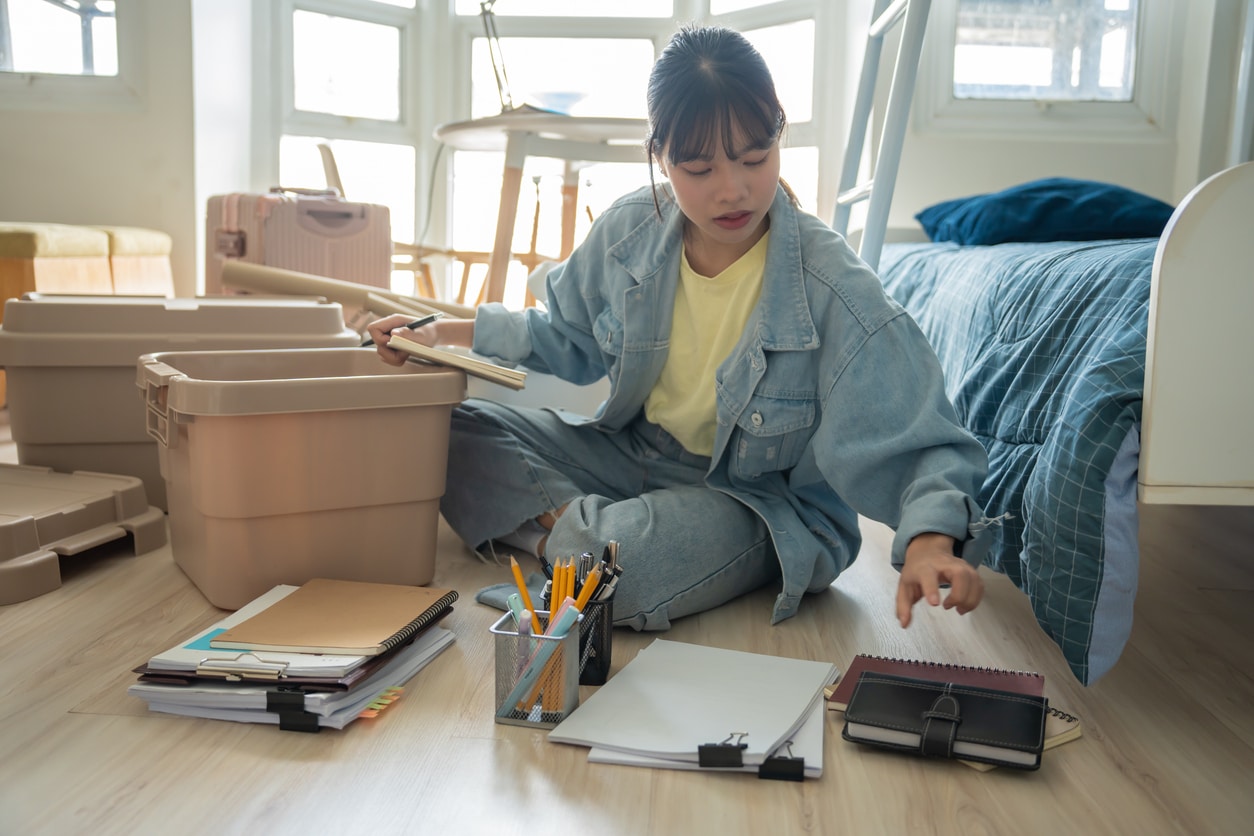  A young woman sits on a bedroom floor, organizing her things as she plans on moving for grad school