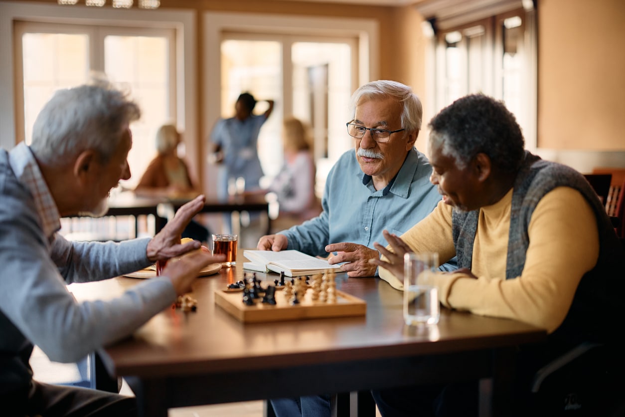 Three senior men playing a game of chess at a table in a social club setting after moving for retirement