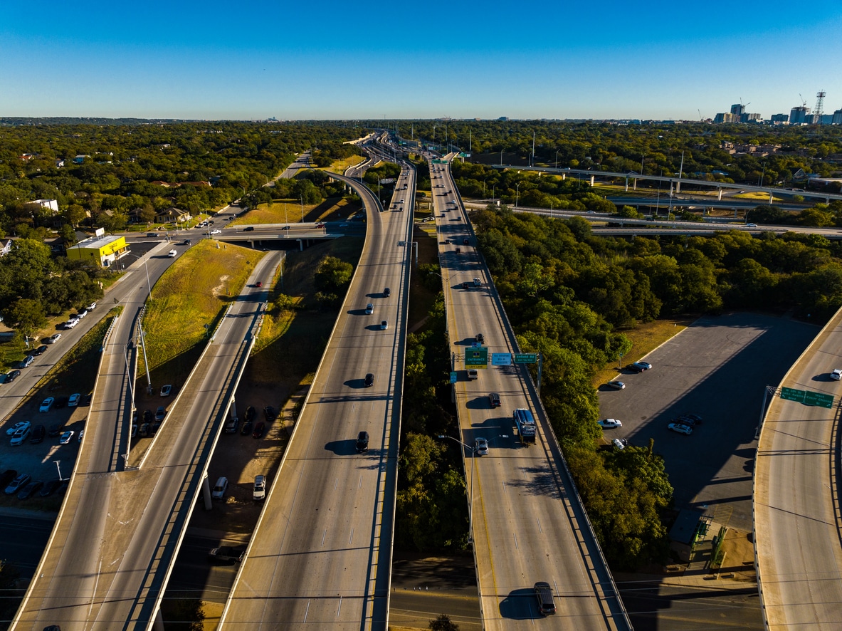 Aerial view of several multi-lane highway flyovers and interchanges in Austin, Texas, surrounded by lush green trees