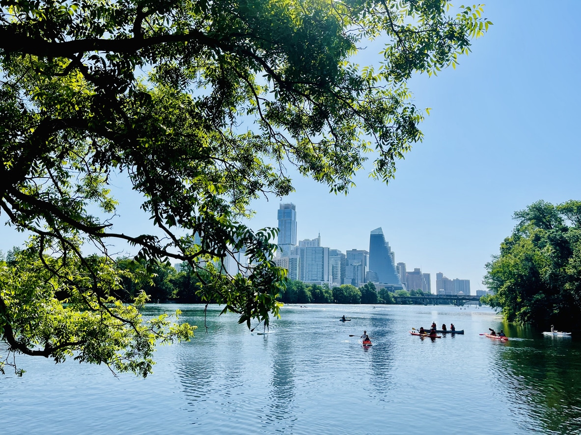 Kayaks and paddleboards on Lady Bird Lake with a view of the downtown Austin skyline framed by tree branches