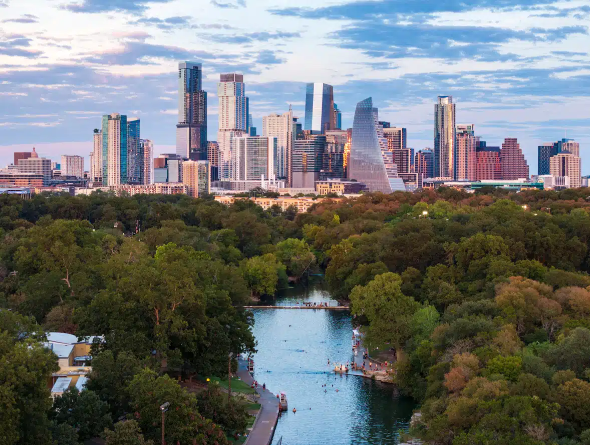 An aerial view of the Austin skyline at sunset overlooking the turquoise waters and swimmers at Barton Springs Pool