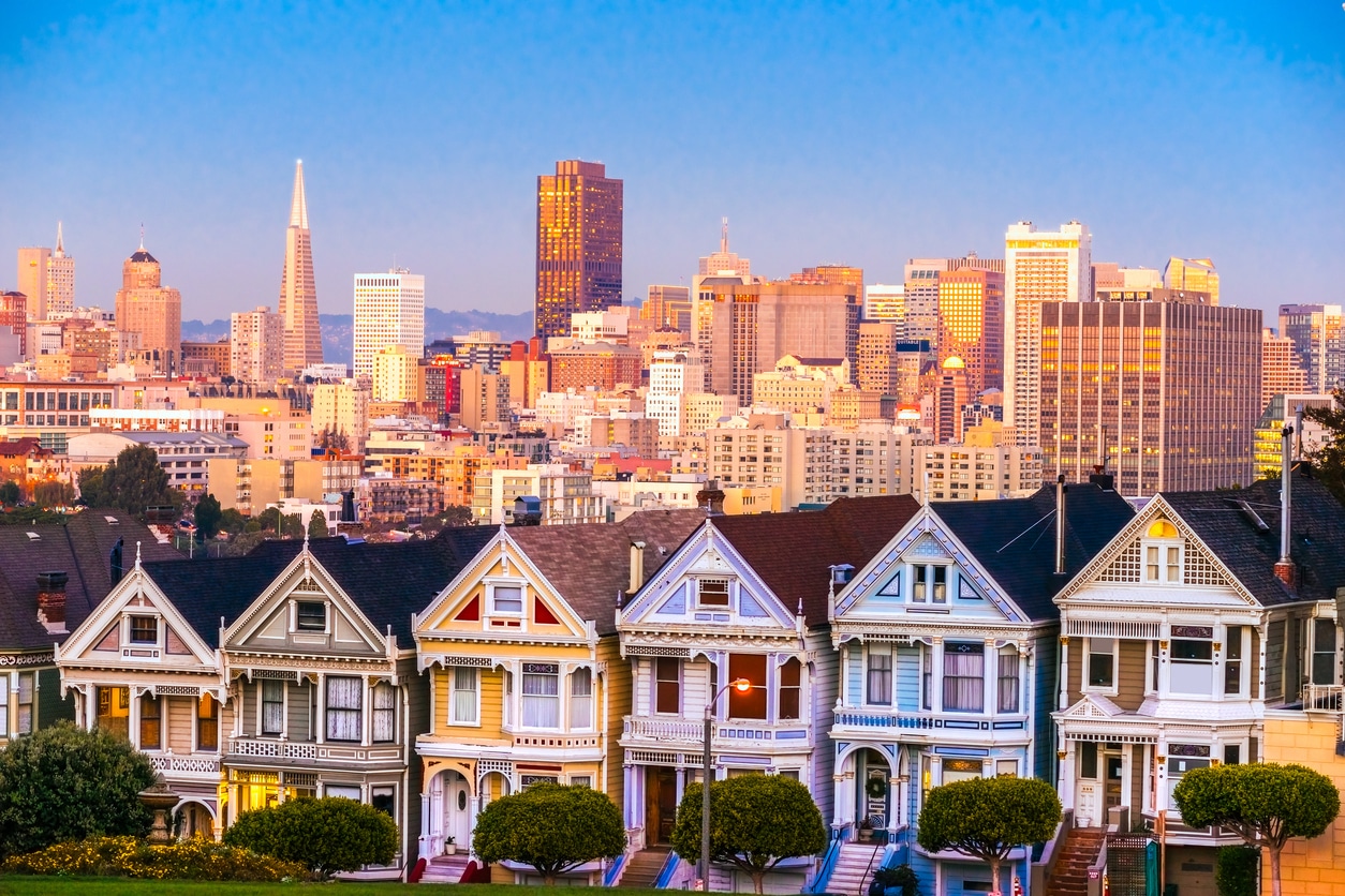 San Francisco's Painted Ladies Victorian houses in the foreground with the glowing downtown skyline at sunset