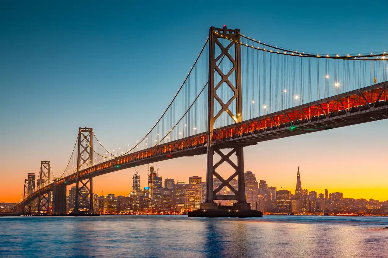 The San Francisco-Oakland Bay Bridge illuminated at sunset with the city skyline in the background