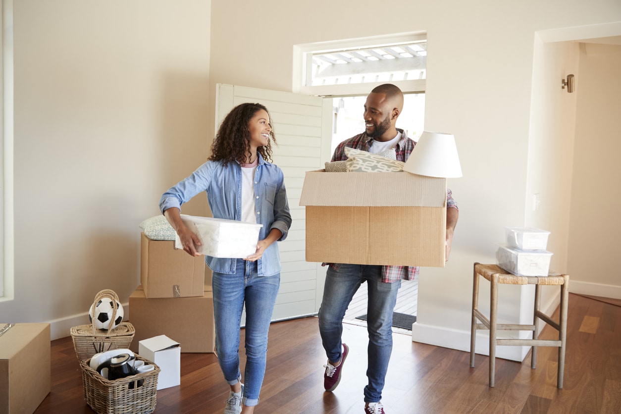 A happy couple carries moving boxes through the entryway of their new home.