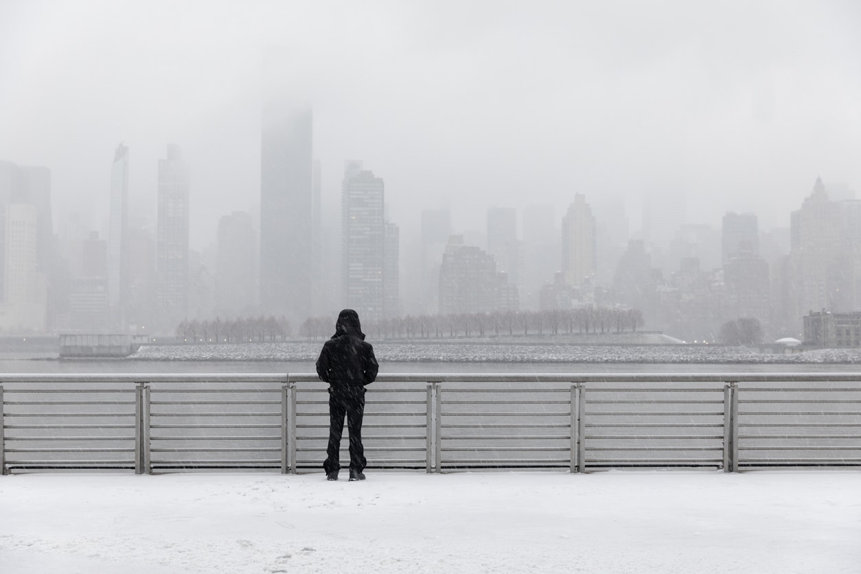 A person in black winter gear looks out at a snow-covered New York City skyline