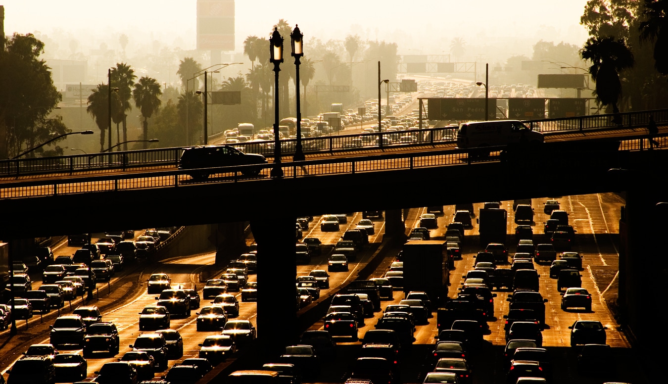 Heavy highway traffic in Los Angeles during a golden sunset, with silhouettes of palm trees in the background