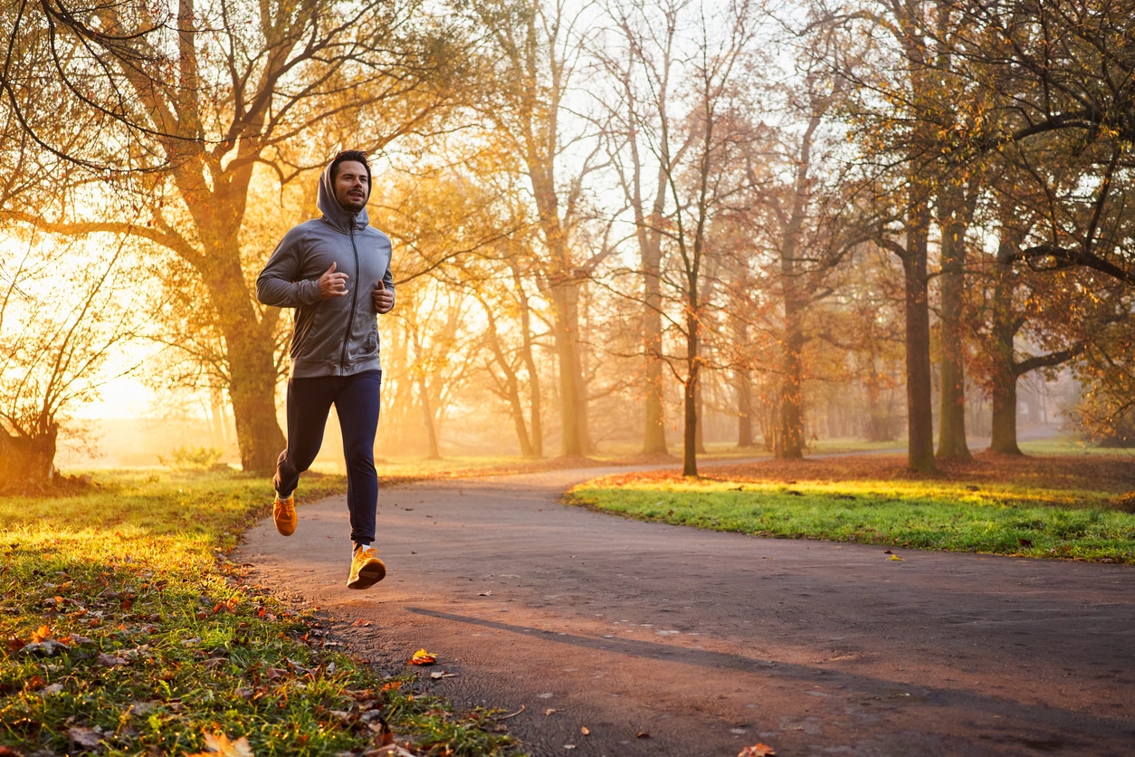 A man in a gray hoodie jogs on a park path during a golden autumn sunrise after relocating for health and well-being
