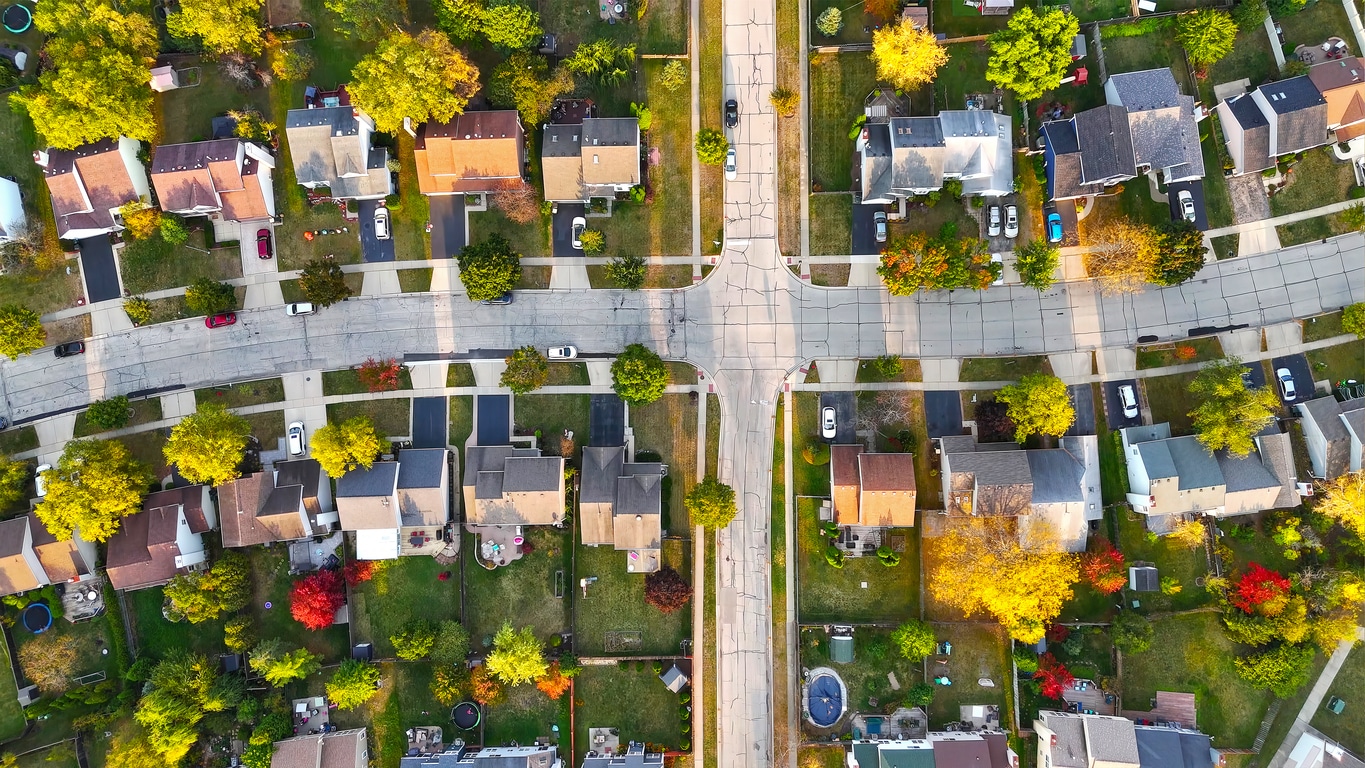 Aerial view of a quiet suburban neighborhood with rows of houses, green yards, and trees with autumn colors