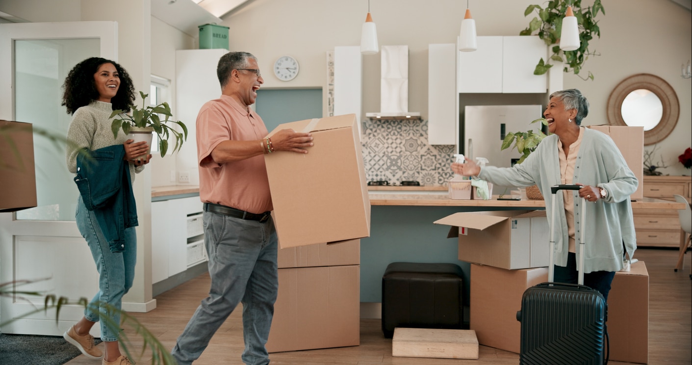 A happy family laughs while carrying moving boxes into a modern kitchen while moving back home